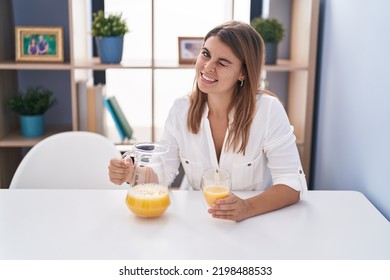 Young Hispanic Woman Drinking Glass Of Orange Juice Winking Looking At The Camera With Sexy Expression, Cheerful And Happy Face. 