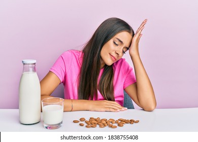 Young Hispanic Woman Drinking Healthy Almond Milk Sitting On The Table Surprised With Hand On Head For Mistake, Remember Error. Forgot, Bad Memory Concept. 