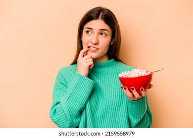 Young Hispanic Woman Eating Cereals Isolated On Beige Background Relaxed Thinking About Something Looking At A Copy Space.