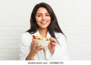 Young hispanic woman eating a fruit bowl on the bed