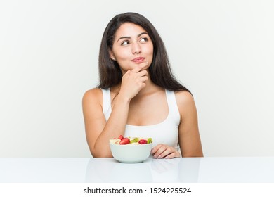 Young hispanic woman eating a fruit bowl looking sideways with doubtful and skeptical expression. - Powered by Shutterstock