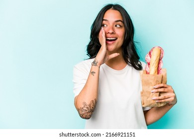 Young Hispanic Woman Eating A Sandwich Isolated On Blue Background Is Saying A Secret Hot Braking News And Looking Aside