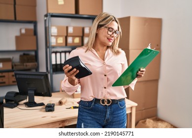 Young Hispanic Woman Ecommerce Business Worker Holding Calculator And Clipboard At Office