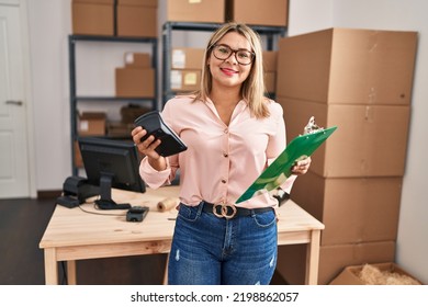 Young Hispanic Woman Ecommerce Business Worker Holding Calculator And Clipboard At Office