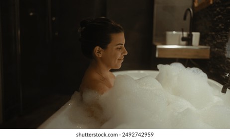 Young hispanic woman enjoying a relaxing bubble bath in a dimly lit home bathroom - Powered by Shutterstock