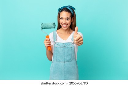young hispanic woman feeling proud,smiling positively with thumbs up and painting a wall - Powered by Shutterstock