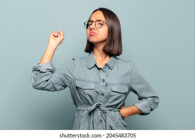 Young Hispanic Woman Feeling Serious, Strong And Rebellious, Raising Fist Up, Protesting Or Fighting For Revolution