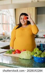 Young hispanic woman having fun in her kitchen-happy woman enjoying healthy cooking-Happy young girl with an tomatoe