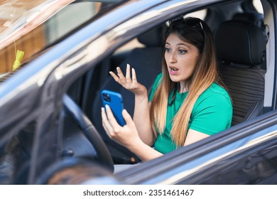 Young hispanic woman having video call sitting on car at street - Powered by Shutterstock