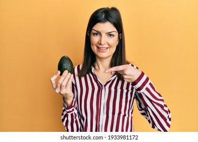 Young Hispanic Woman Holding Avocado Smiling Happy Pointing With Hand And Finger 