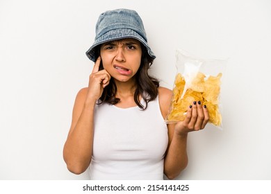 Young Hispanic Woman Holding A Bag Of Chips Isolated On White Background Covering Ears With Hands.