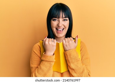 Young Hispanic Woman Holding Book Smiling And Laughing Hard Out Loud Because Funny Crazy Joke. 