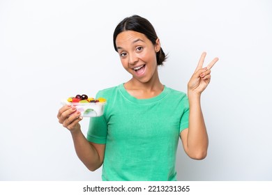 Young Hispanic Woman Holding A Bowl Of Fruit Isolated On White Background Smiling And Showing Victory Sign