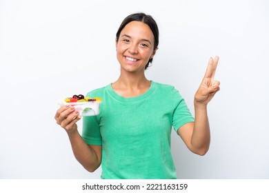 Young Hispanic Woman Holding A Bowl Of Fruit Isolated On White Background Smiling And Showing Victory Sign