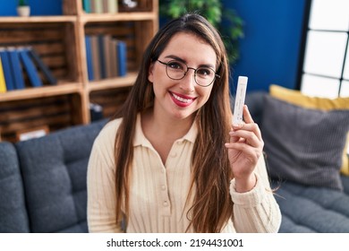 Young hispanic woman holding coronavirus test looking positive and happy standing and smiling with a confident smile showing teeth  - Shutterstock ID 2194431001