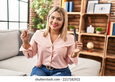 Young Hispanic Woman Holding Eye Lashes Curler And Nail File Smiling With A Happy And Cool Smile On Face. Showing Teeth. 