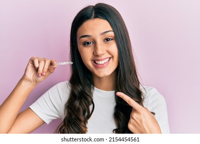 Young hispanic woman holding invisible aligner orthodontic smiling happy pointing with hand and finger 