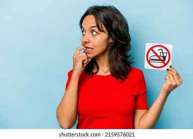 Young Hispanic Woman Holding No Eating Sign Isolated On Blue Background Relaxed Thinking About Something Looking At A Copy Space.