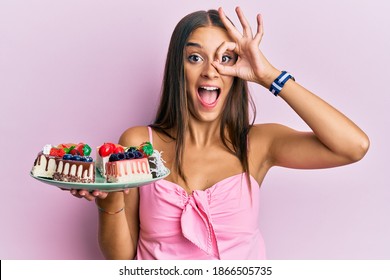 Young Hispanic Woman Holding Plate With Cheesecake Smiling Happy Doing Ok Sign With Hand On Eye Looking Through Fingers 