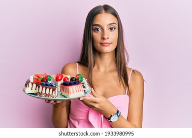 Young Hispanic Woman Holding Plate With Cheesecake Thinking Attitude And Sober Expression Looking Self Confident 