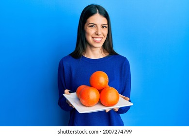 Young Hispanic Woman Holding Plate With Fresh Oranges Smiling With A Happy And Cool Smile On Face. Showing Teeth. 