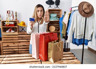 Young Hispanic Woman Holding Shopping Bags And Credit Card At Clothing Store Doing Stop Sing With Palm Of The Hand. Warning Expression With Negative And Serious Gesture On The Face. 