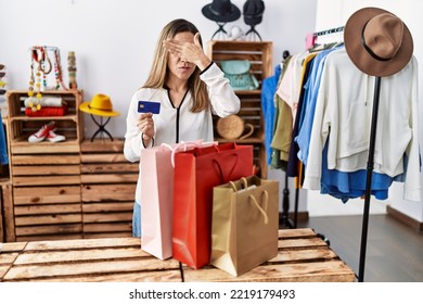 Young Hispanic Woman Holding Shopping Bags And Credit Card At Clothing Store Covering Eyes With Hand, Looking Serious And Sad. Sightless, Hiding And Rejection Concept 