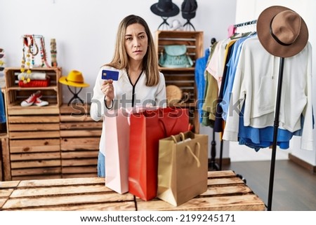 Young hispanic woman holding shopping bags and credit card at clothing store looking sleepy and tired, exhausted for fatigue and hangover, lazy eyes in the morning. 