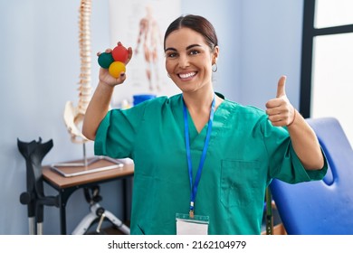 Young hispanic woman holding small balls to train hand muscle smiling happy and positive, thumb up doing excellent and approval sign 