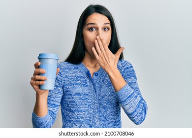 Young hispanic woman holding take away coffee covering mouth with hand, shocked and afraid for mistake. surprised expression 