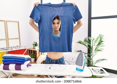 Young Hispanic Woman Ironing Holding Burned Iron Shirt At Laundry Room Depressed And Worry For Distress, Crying Angry And Afraid. Sad Expression. 