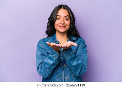 Young Hispanic Woman Isolated On Purple Background Holding Something With Palms, Offering To Camera.