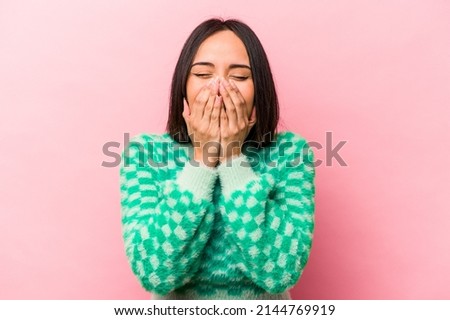 Young hispanic woman isolated on pink background laughing about something, covering mouth with hands.