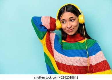 Young Hispanic Woman Listening To Music Isolated On Blue Background Touching Back Of Head, Thinking And Making A Choice.