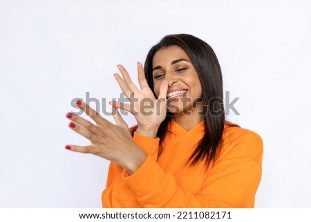 Young Hispanic woman making long nose gesture. Female model in orange hoodie grimacing and laughing. Portrait, studio shot, grimacing concept