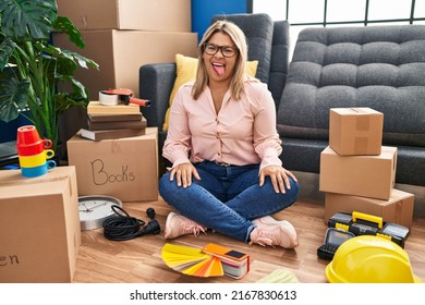 Young Hispanic Woman Moving To A New Home Sitting On The Floor Sticking Tongue Out Happy With Funny Expression. Emotion Concept. 