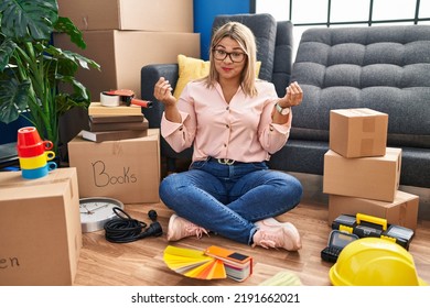 Young Hispanic Woman Moving To A New Home Sitting On The Floor Doing Money Gesture With Hands, Asking For Salary Payment, Millionaire Business 