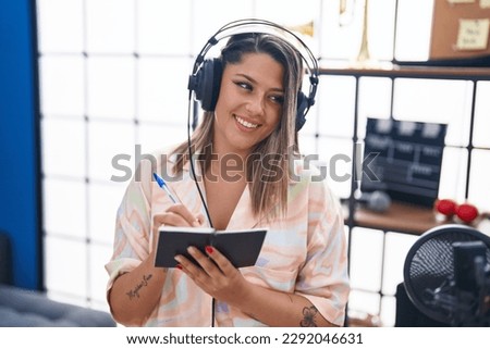 Young hispanic woman musician listening to music composing song at music studio