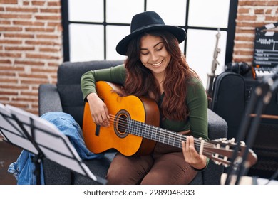 Young hispanic woman musician playing classical guitar at music studio - Powered by Shutterstock