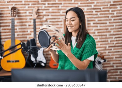 Young hispanic woman musician playing tambourine at music studio - Powered by Shutterstock