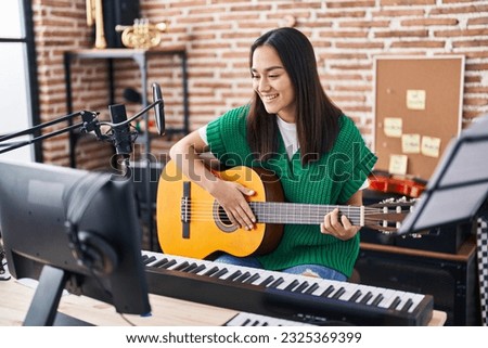 Young hispanic woman musician playing classical guitar at music studio