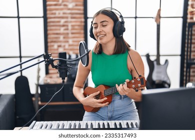 Young hispanic woman musician singing song playing ukelele at music studio
