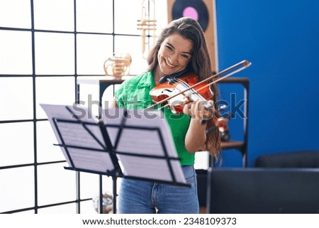Young hispanic woman musician smiling confident playing violin at music studio