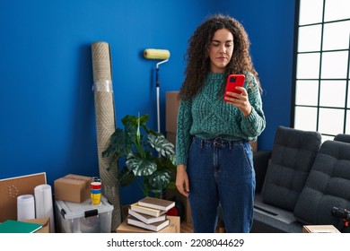 Young Hispanic Woman At New Home Using Smartphone Thinking Attitude And Sober Expression Looking Self Confident 