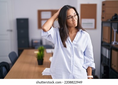 Young hispanic woman at the office confuse and wondering about question. uncertain with doubt, thinking with hand on head. pensive concept. 