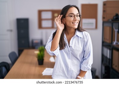 Young Hispanic Woman At The Office Smiling With Hand Over Ear Listening An Hearing To Rumor Or Gossip. Deafness Concept. 