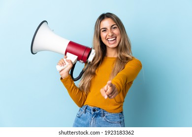 Young hispanic woman over isolated blue background holding a megaphone and smiling while pointing to the front