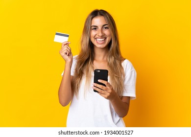 Young Hispanic Woman Over Isolated Yellow Background Buying With The Mobile With A Credit Card