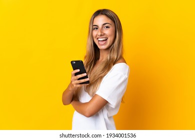Young hispanic woman over isolated yellow background holding a mobile phone and with arms crossed