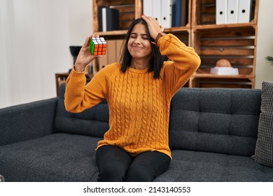 Young Hispanic Woman Playing Colorful Puzzle Cube Intelligence Game Stressed And Frustrated With Hand On Head, Surprised And Angry Face 